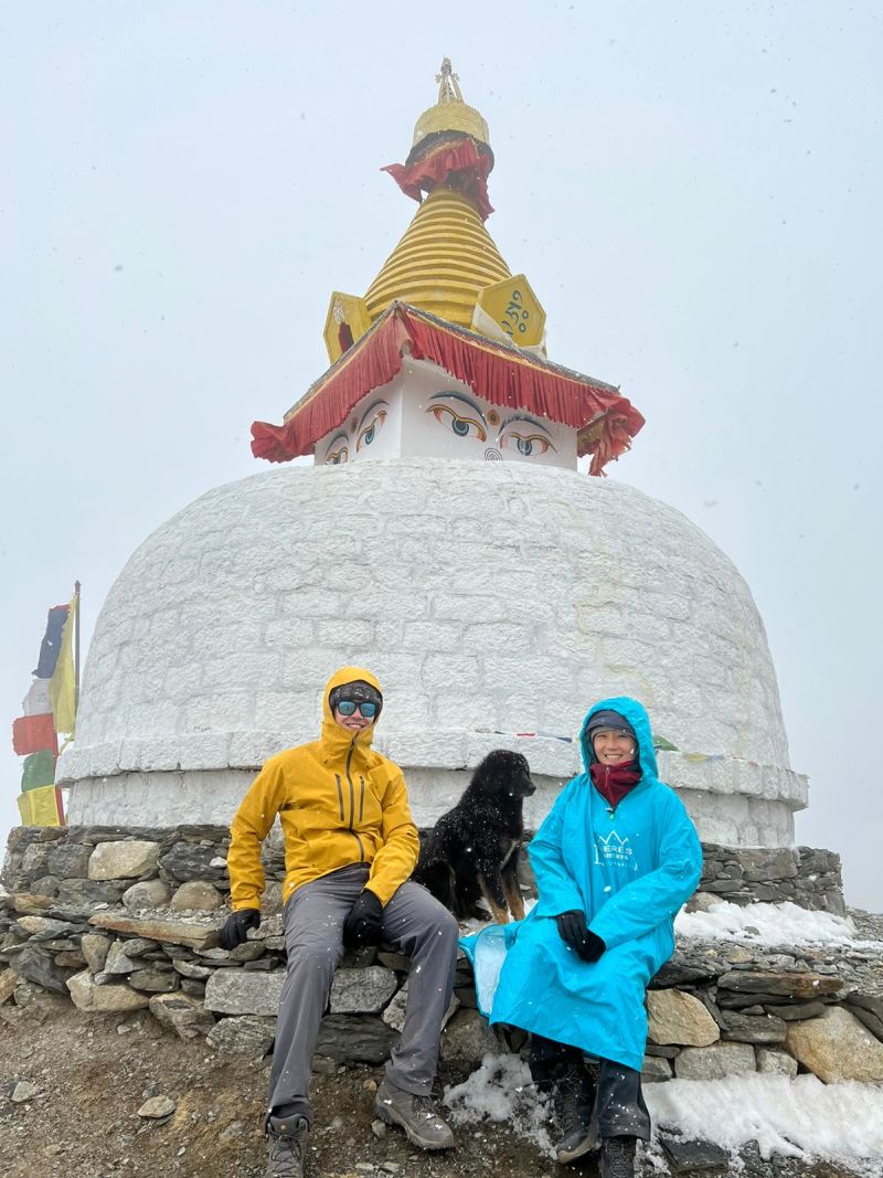 Nepal EBC trek, trekkers sitting with dog by stupa in mist