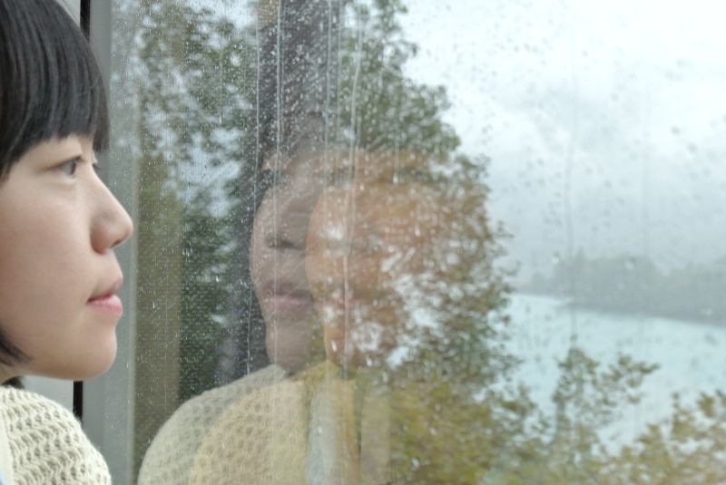 Asian woman looking out of train window at rainy landscape