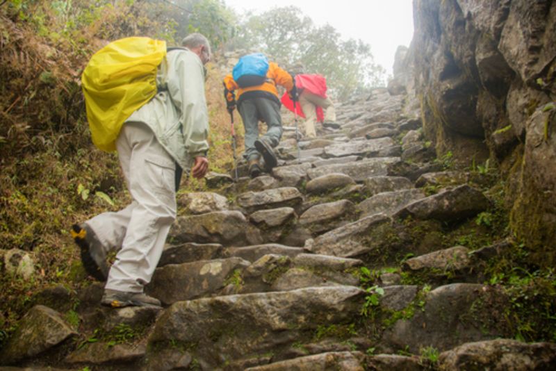 Three hikers on the Inca trail, in the rain and fog near the Puyupatamarca archaeological site, Peru 