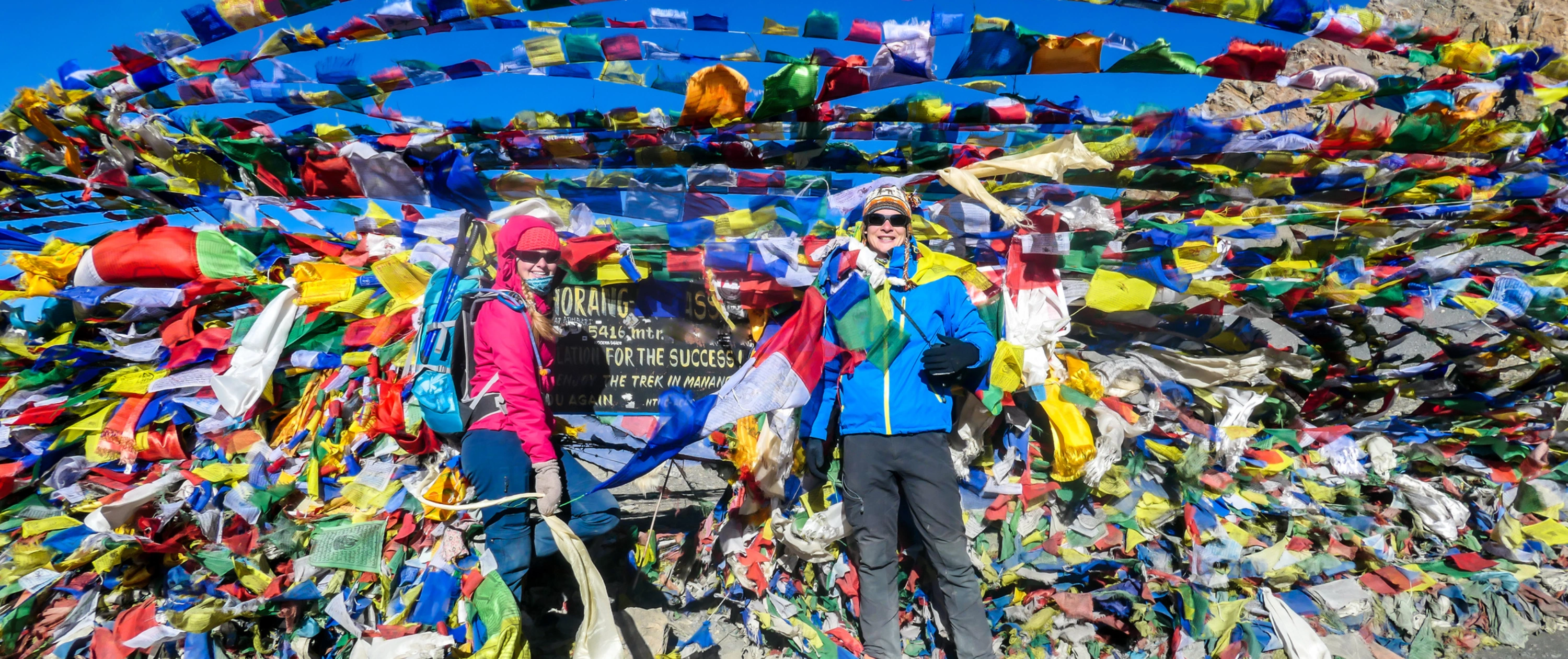 A couple standing between prayer flags at the top of Thorung La Pass, Annapurna Circuit Trek, Nepal 