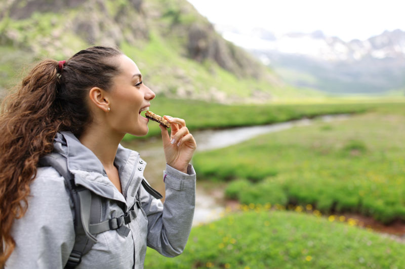Woman eating energy bar in beautiful green countryside with mountains
