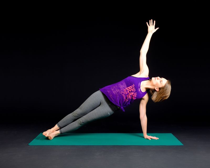 Woman doing a side plank on a green yoga mat
