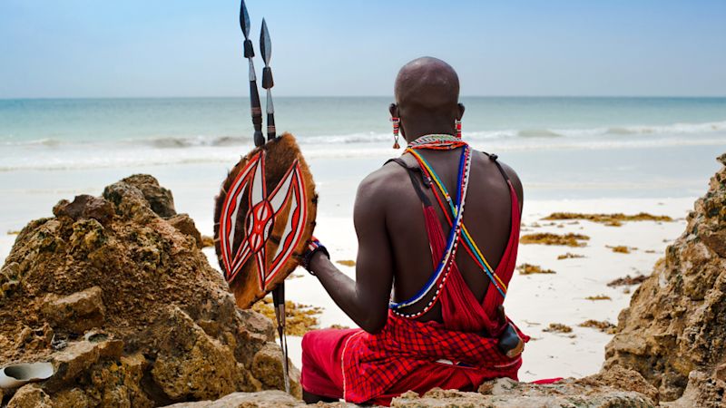 Masai warrior with spears sitting on a rock on a beach in Kenya