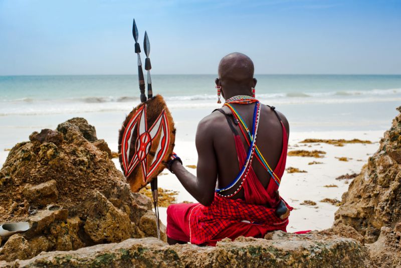Masai warrior with spears sitting on a rock on a beach in Kenya