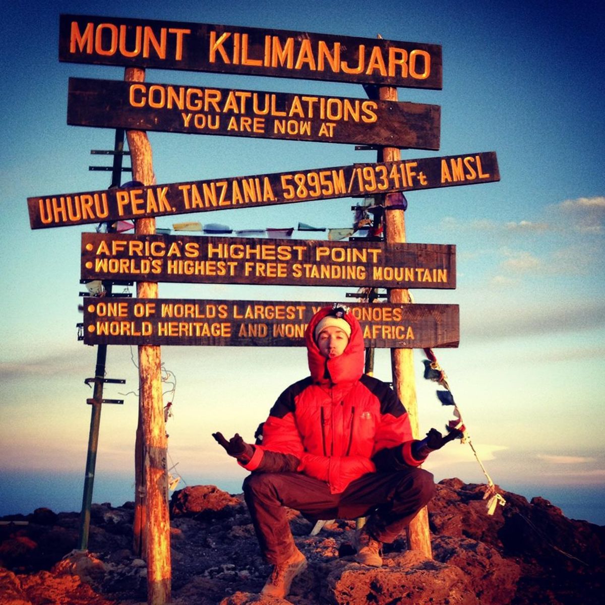 Reto i a zen pose in front of the Uhuru Peak sign on Mt Kilimanjaro