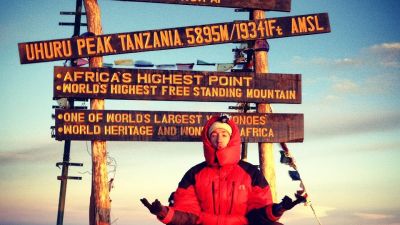 Reto i a zen pose in front of the Uhuru Peak sign on Mt Kilimanjaro