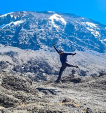 Man leaping in air on Kilimanjaro with Uhuru Peak behind him