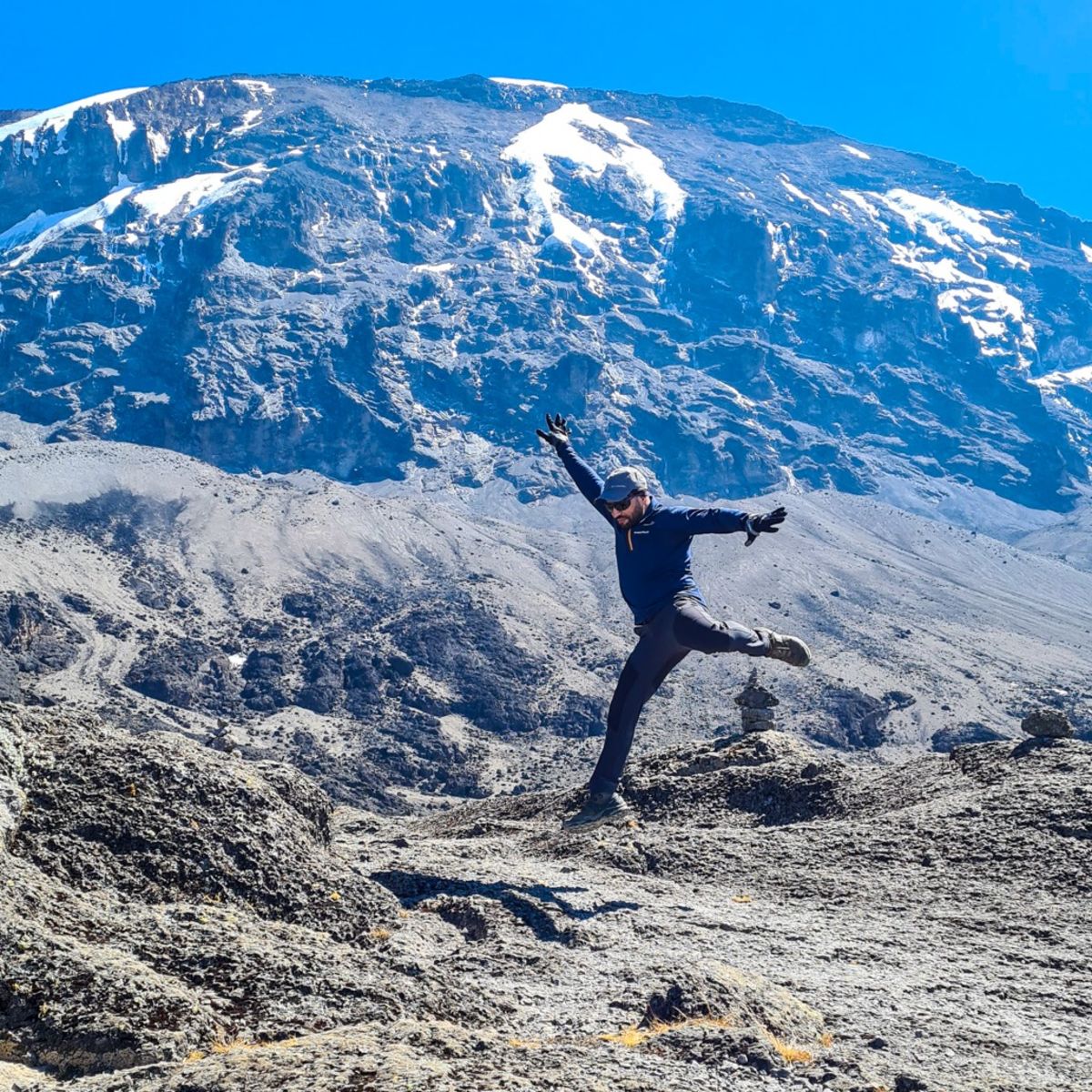 Man leaping in air on Kilimanjaro with Uhuru Peak behind him