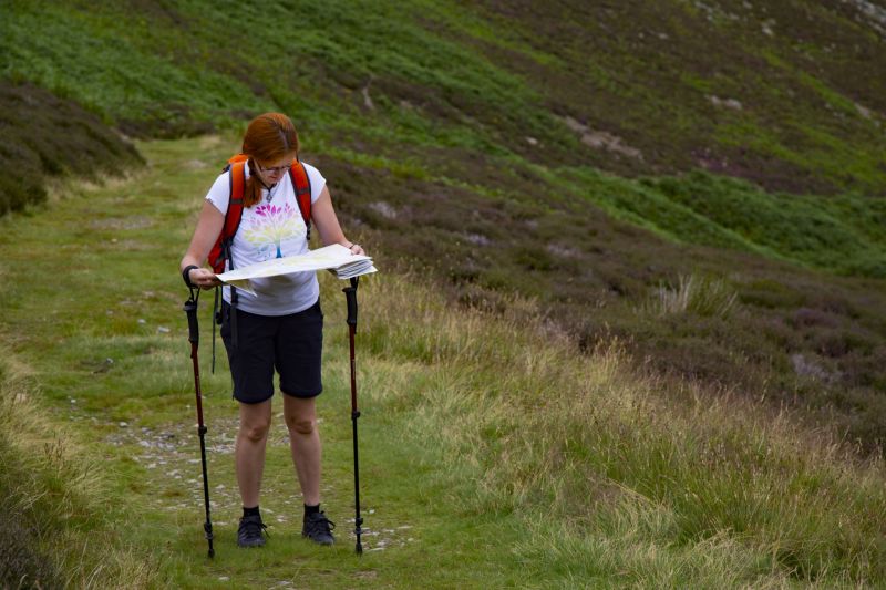 Woman trekker reading map with trekking poles dangling