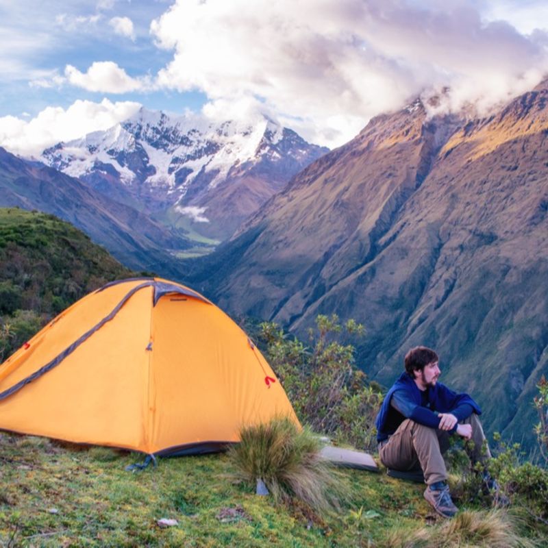Male trekker seated next to tent on Salkantay trek in Andes, Peru