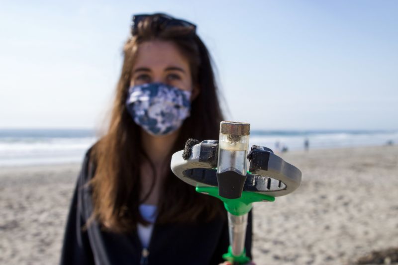 Woman in mask on beach with cleanup tongs