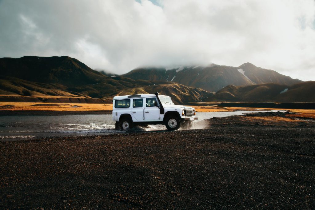 A jeep drives through a river in the barren Landmannalaugar landscape of inner Iceland