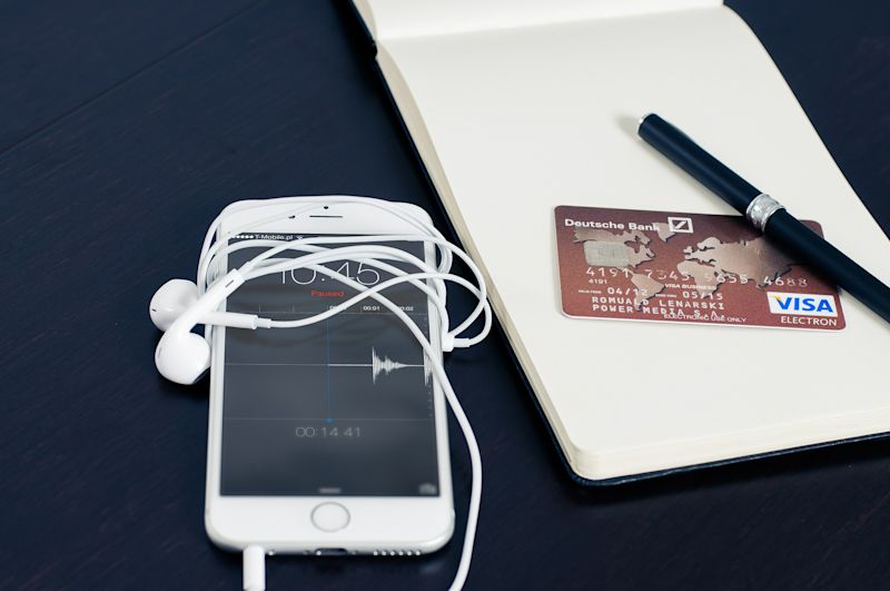 iPhone with earbuds and notepad, bank card and pen