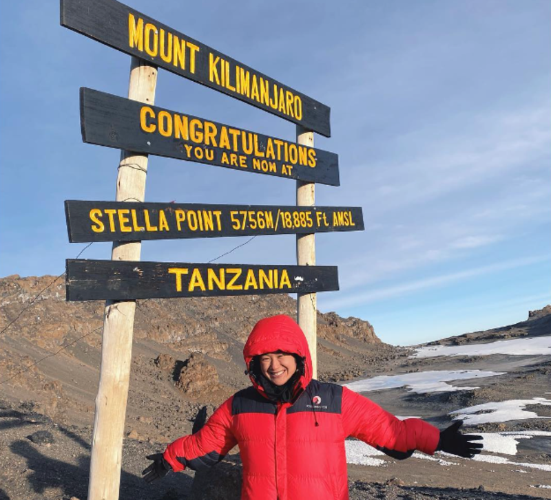 Woman standing by Stella Point sign on Kilimanjaro, August 2022