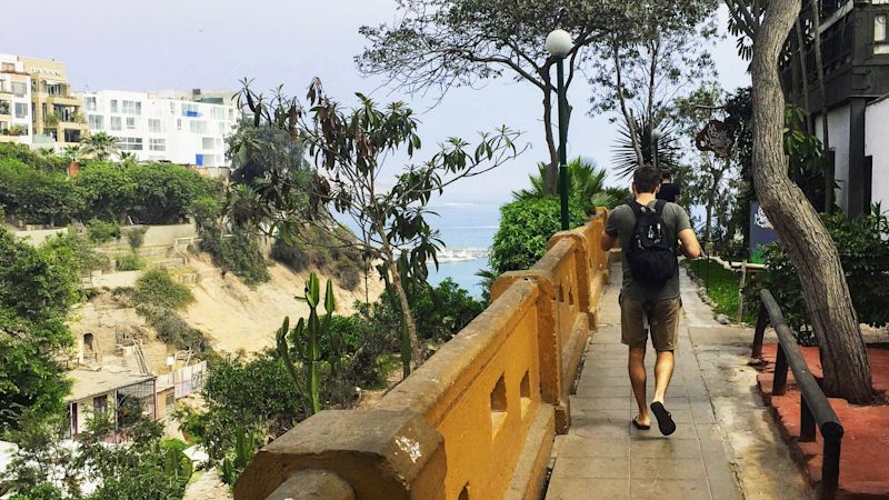 A young male tourist walking along a patio with restaurants high on the hillside of Lima, Peru