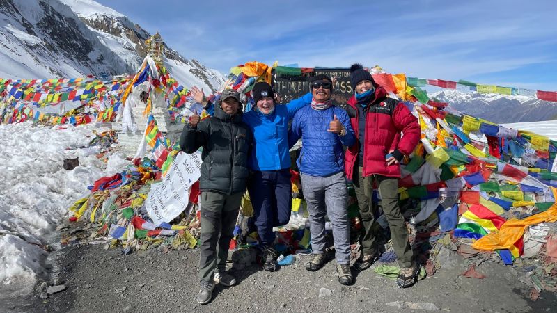 Trekkers smiling in front of Thorung La stone and prayer flags on Thorung La pass on the Annapurna Circuit in Nepal
