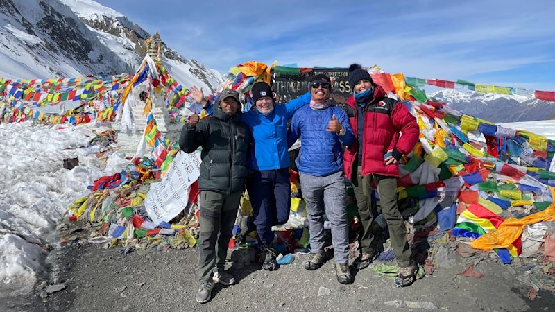 Trekkers smiling in front of Thorung La stone and prayer flags on Thorung La pass on the Annapurna Circuit in Nepal