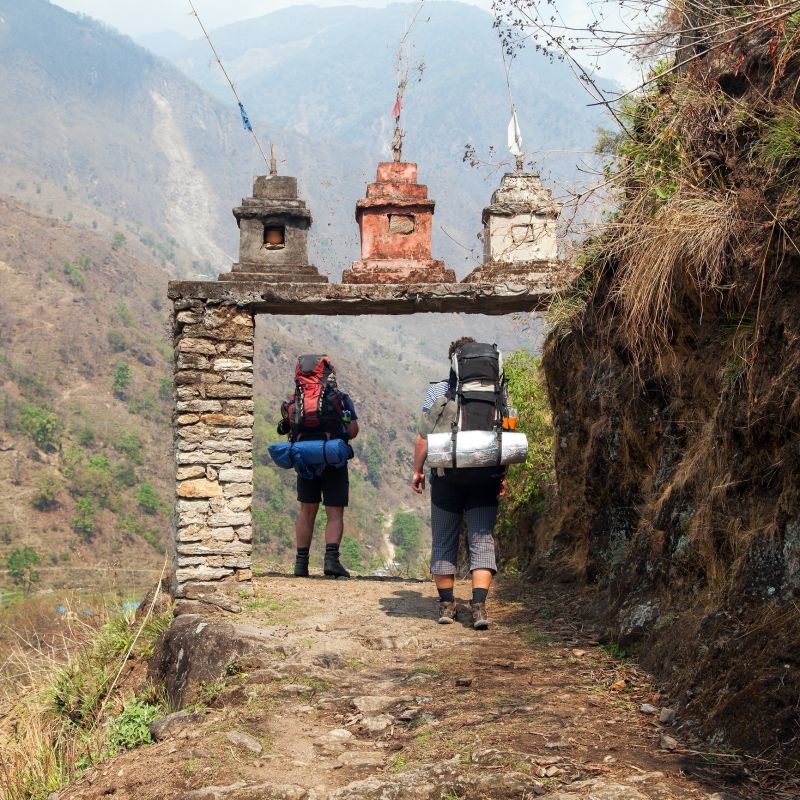 Two male trekkers walk under an arch into a village on the lower Annapurna Circuit in the Himalayas of Nepal