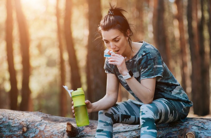 Female hiker seated on log eating a protein bar 
