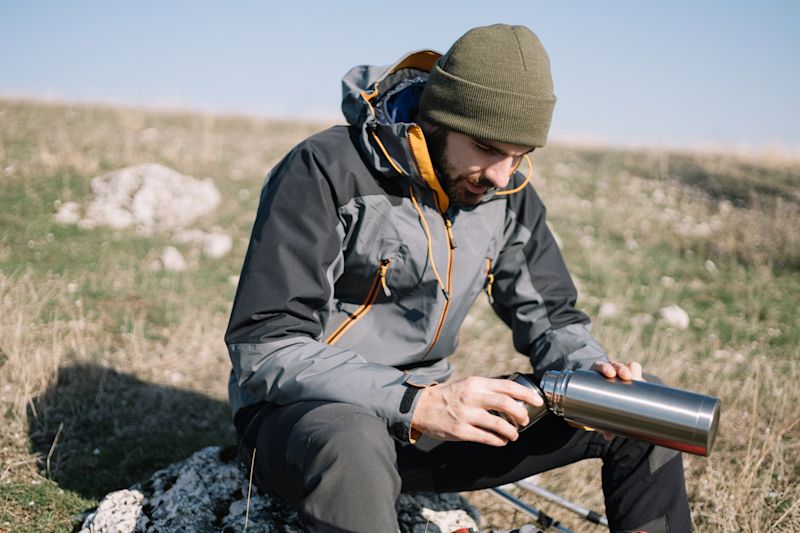 Male trekker seated on rock pouring drink out of flask