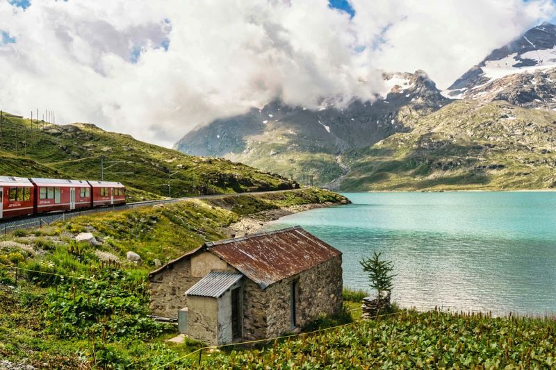 Train passing by a lake and small stone building in the Swiss mountains