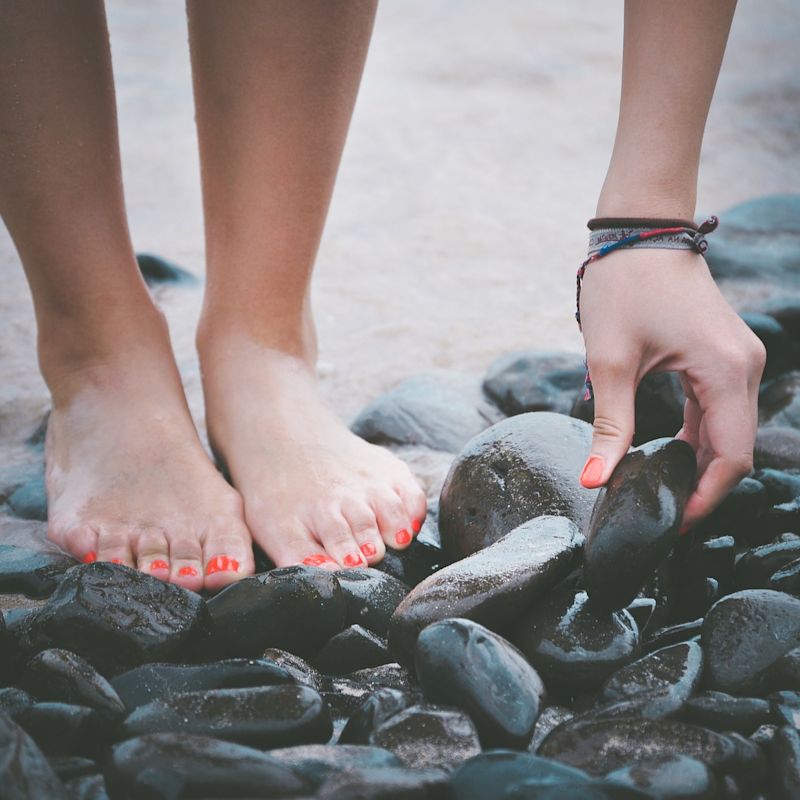 Woman painted nails standing on sand, stones, beach