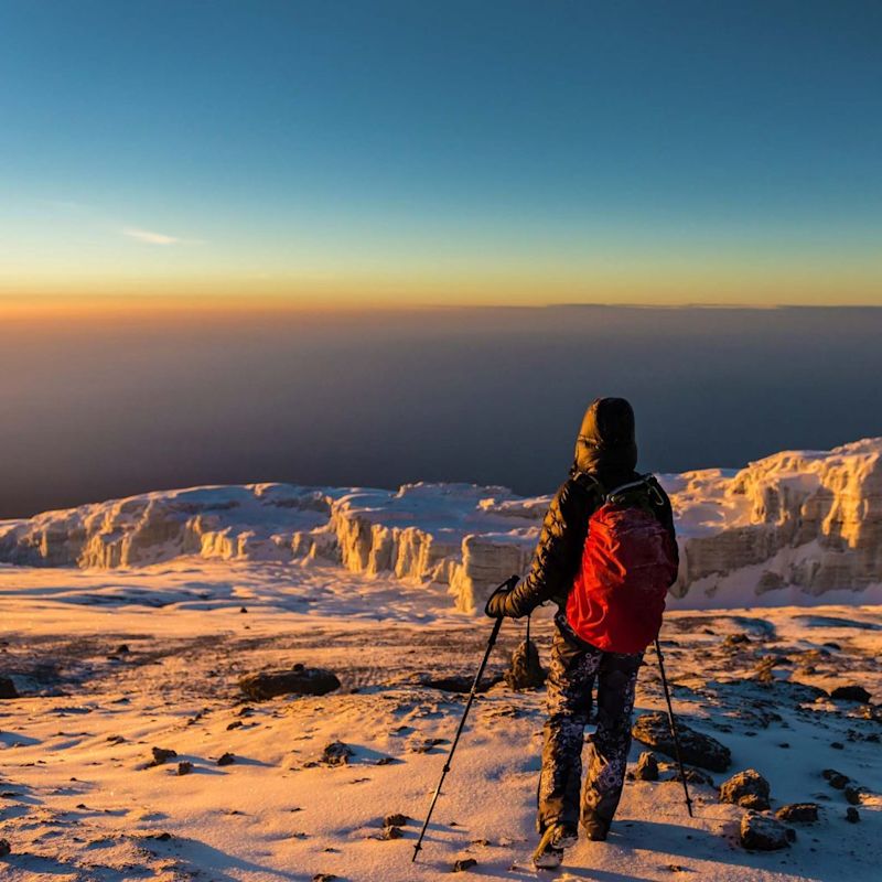 Trekker standing in the snow of Kilimanjaro summit at sunrise