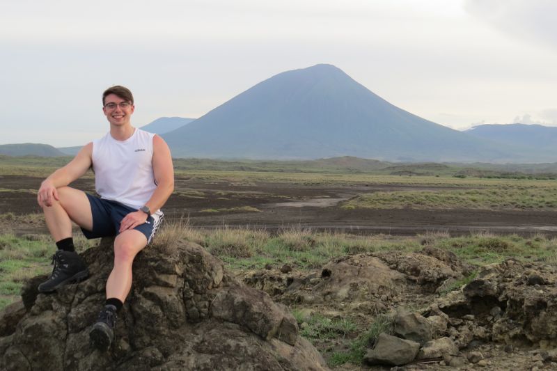 Young man sitting on rock in front of Ol Doinyo Lengai volcano in Lake Natron region of Tanzania