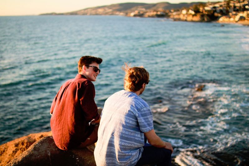Two young men sitting on a rock at the coast