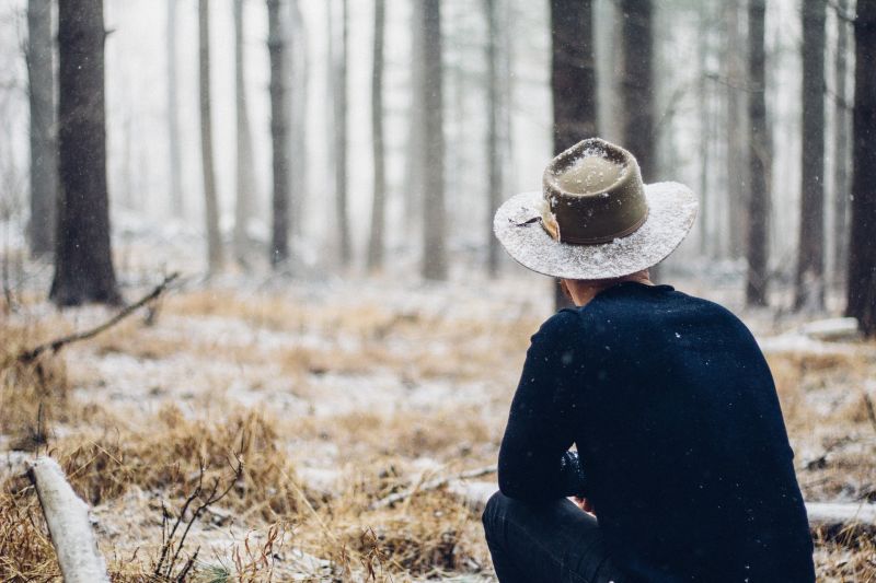 Man in bush hat squatting in woods, wintry landscape, snow