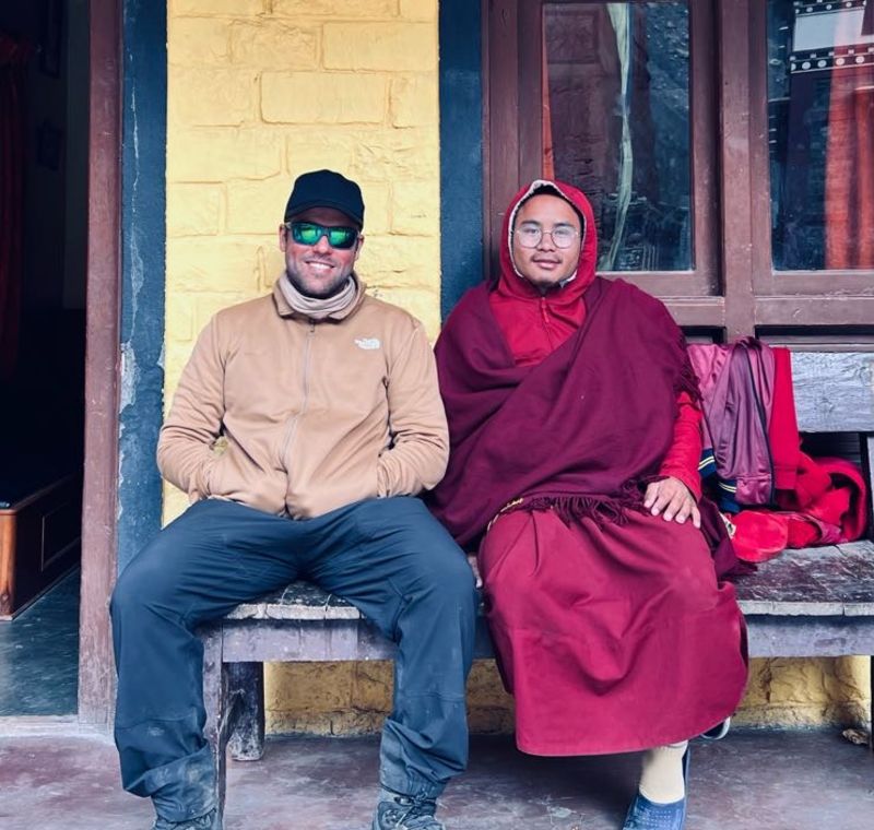 Trekker sitting with Tibetan Buddhist monk on bench on Annapurna Circuit