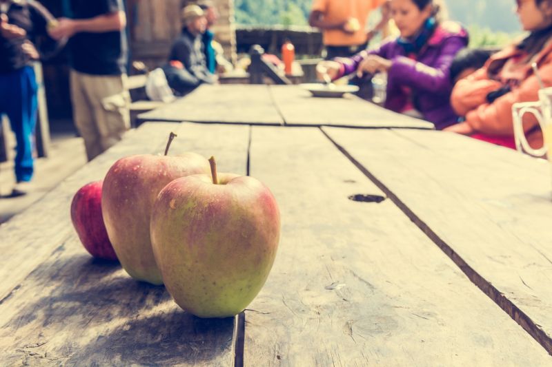 Apples on a wooden table outdoors with seated trekkers in background, annapurna