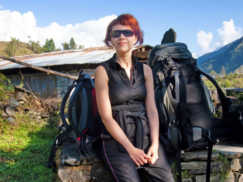 Female redhead trekker on Annapurna Circuit, resting with backpack off, sunglasses on