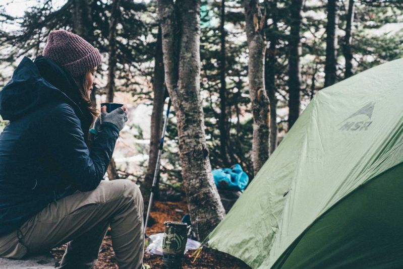 Woman drinking hot beverage in campsite, trekking tips for beginners