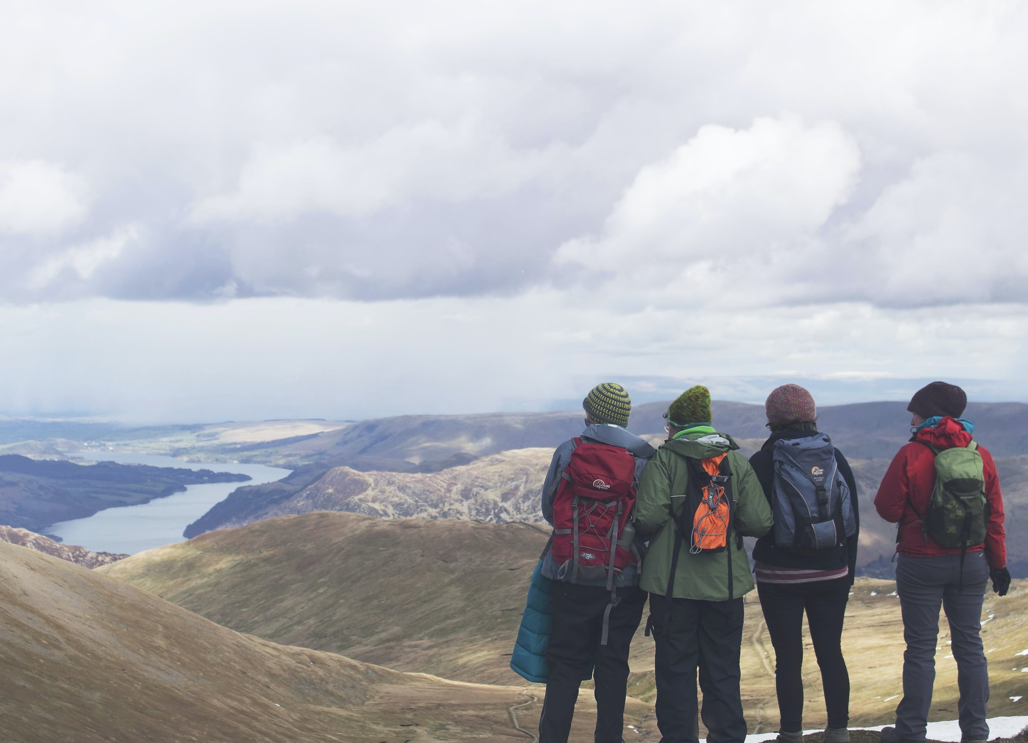 Four women hikers in mountains wearing beanies, jackets and backpacks