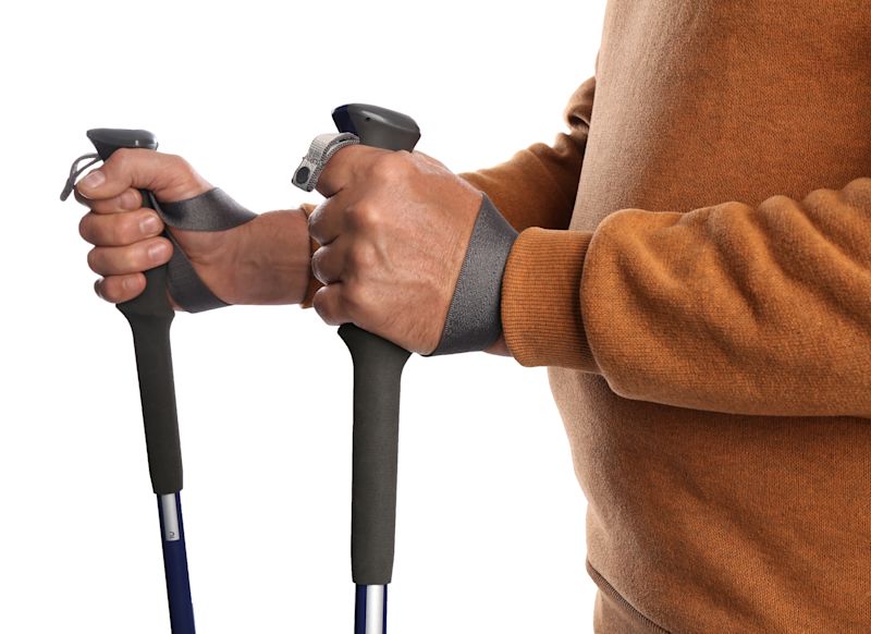 Man holding trekking poles in correct manner against white background