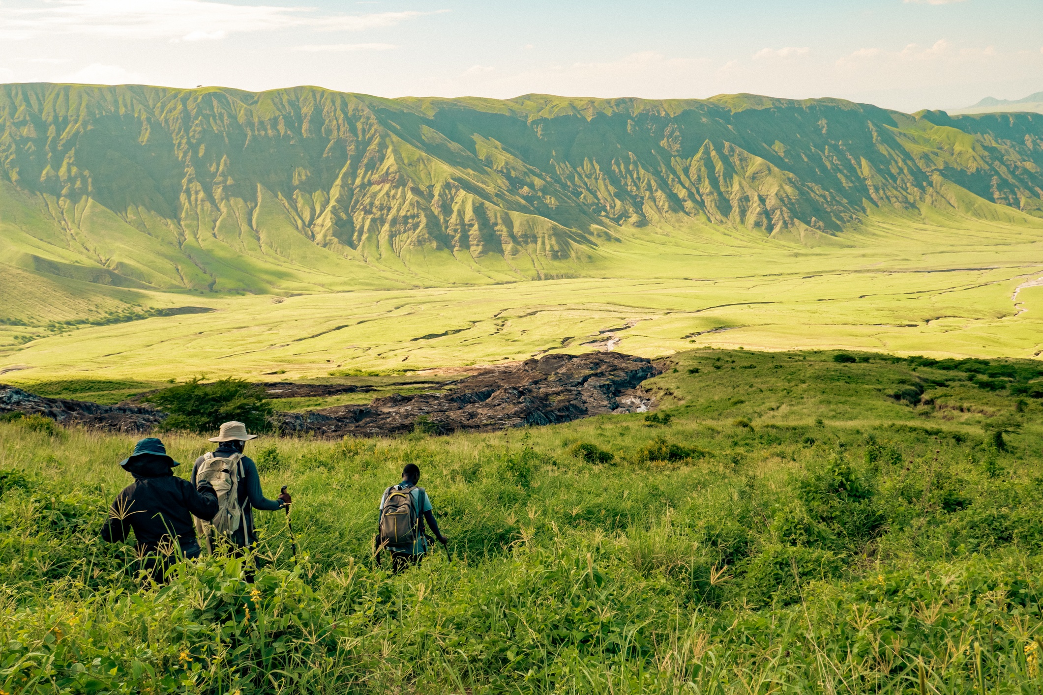 Trekkers descending lower slopes pf Ol Doinyo Lengai with the Great Rift Valley escarpment in the distance