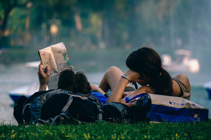 Asian couple with map lying on backpacks on grass