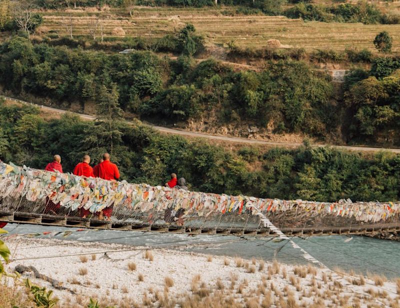 Monks walk across Punakha Bridge, festooned with countless prayer flags