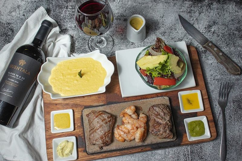 Aerial view of meat course served on wood board with wine bottle and wine glass and cutlery at Uchu Peruvian Steakhouse in Cusco, Peru