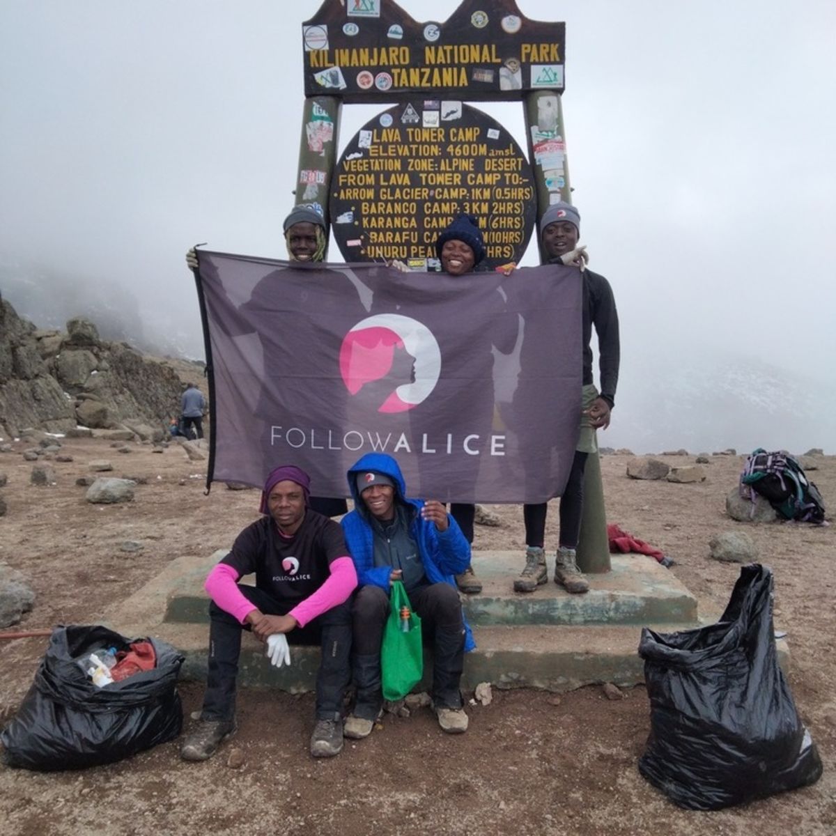 Group of men and women holding Follow Alice flag on Mt Kilimanjaro with full rubbish bags