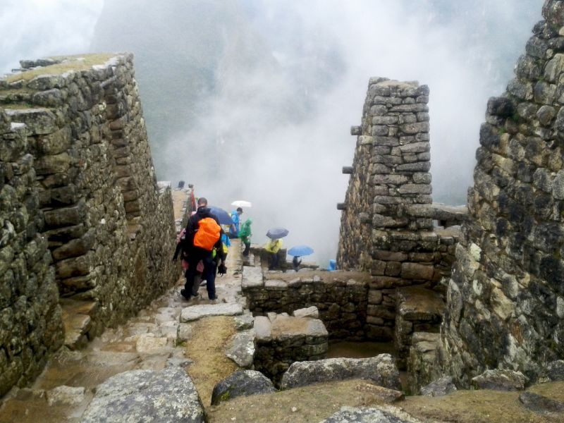 Trekkers with umbrellas and rain jackets in misty and rainy Machu Picchu ruins, Peru
