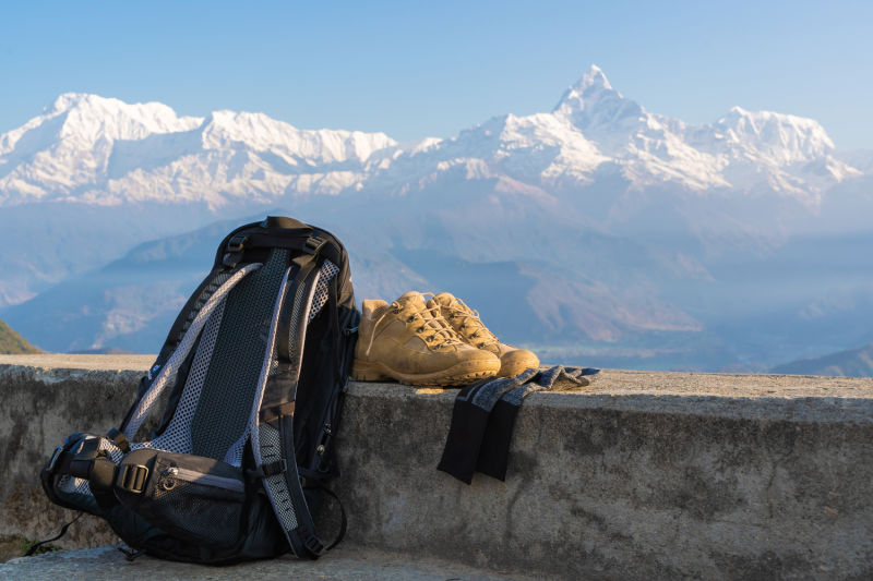 Backpack, hiking boots and socks on low wall with Annapurna mountains behind, Nepal
