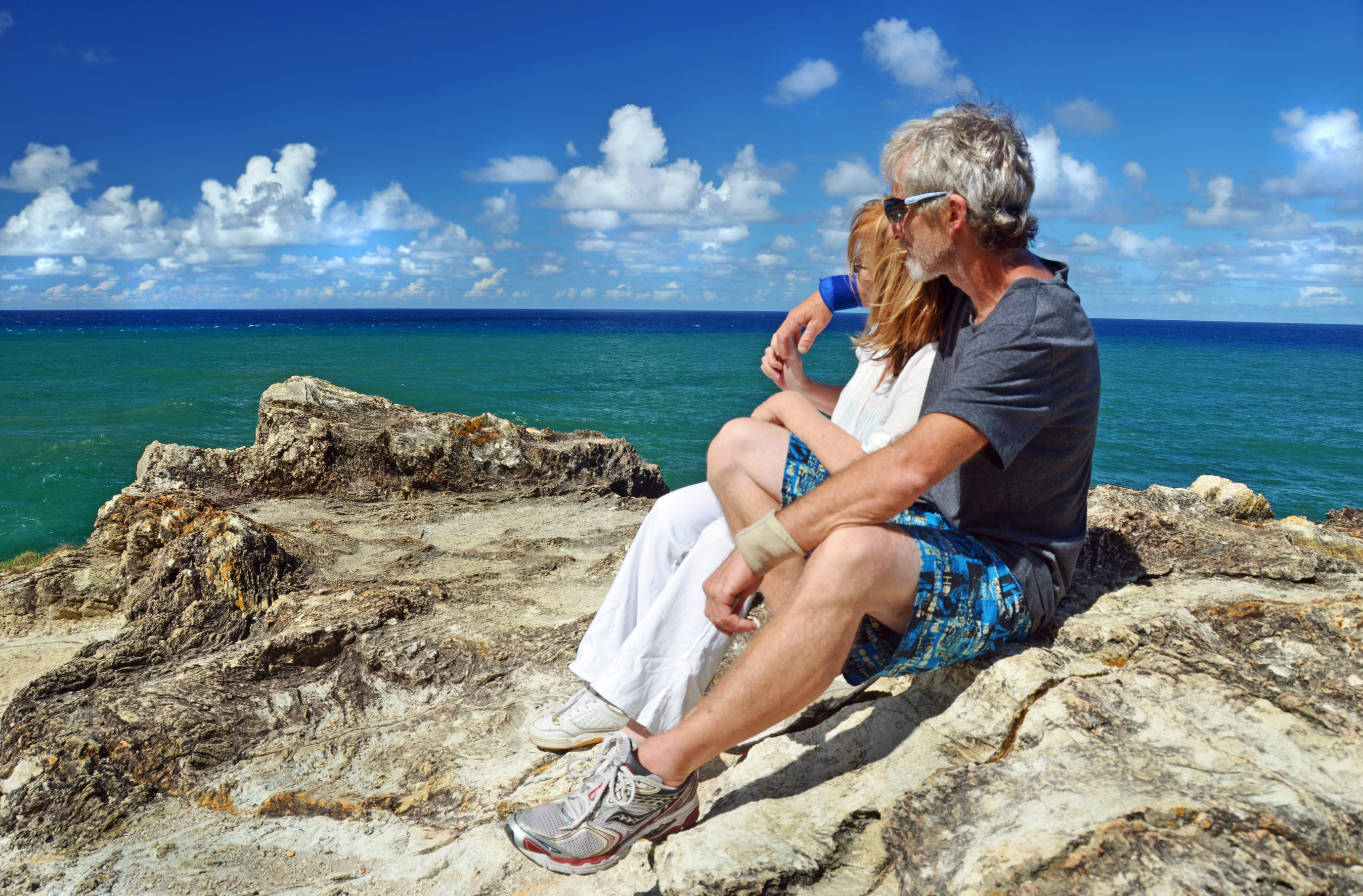 senior couple resting after hiking to cliff top tropical island.