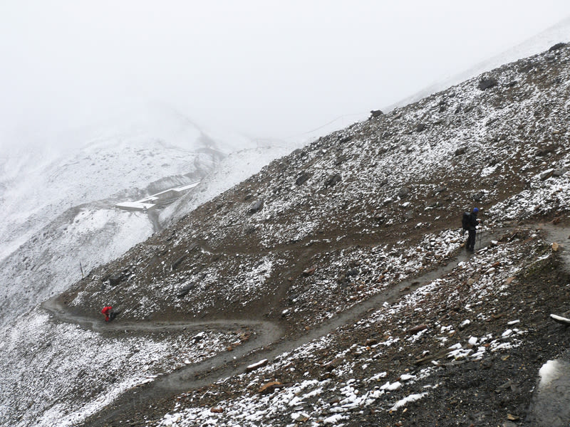 Two trekkers hiking in snowy and misty conditions on the Annapurna Circuit on their way to Thorung La