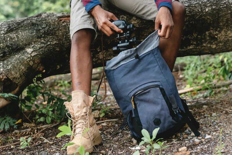 Man pulling camera out of backpack while sitting on fallen tree trunk