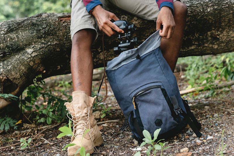 Man pulling camera out of backpack while sitting on fallen tree trunk