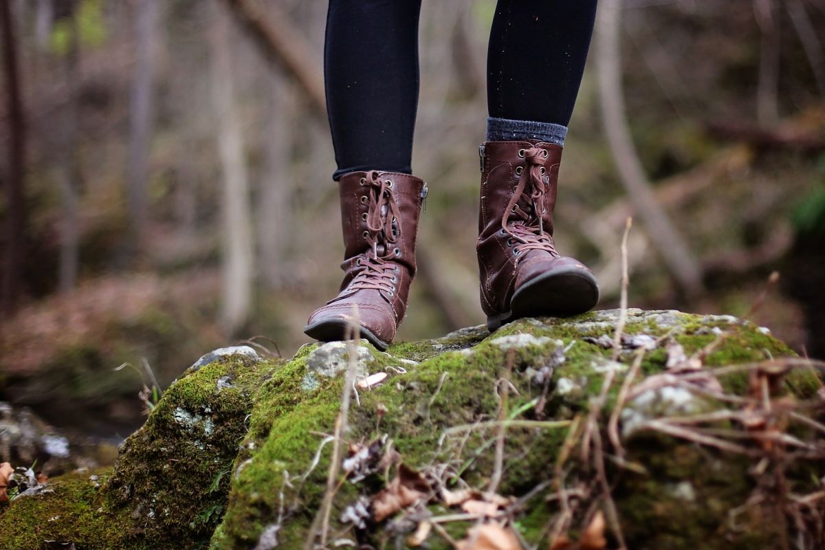 Close up of a woman's lower legs and hiking boots while she stands on a mossy rock in the forest