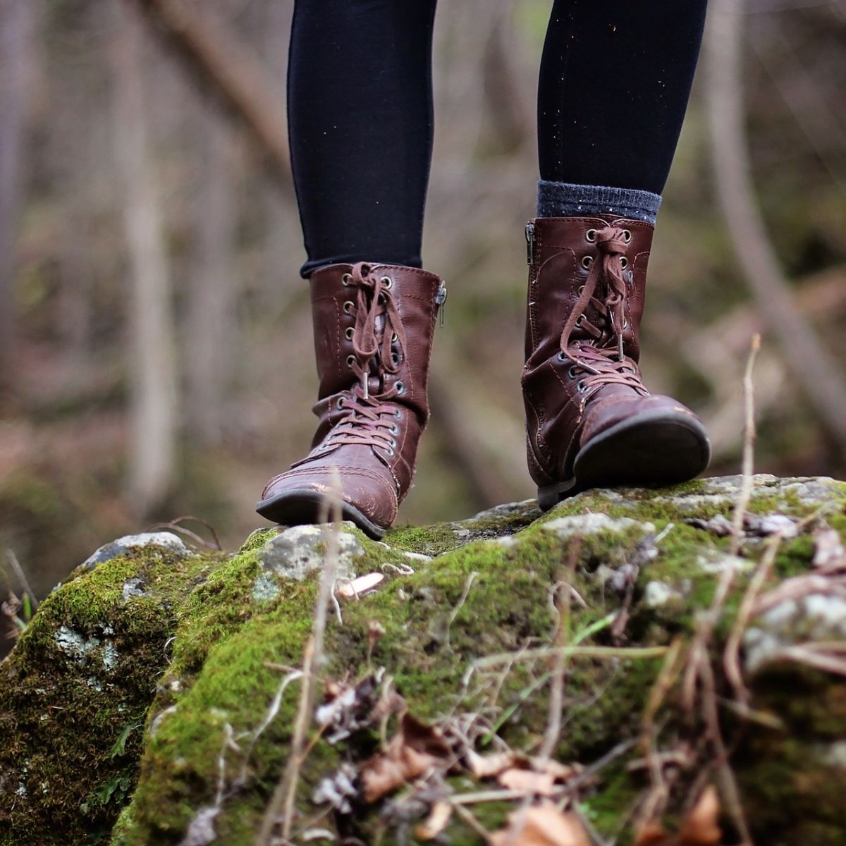 Close up of a woman's lower legs and hiking boots while she stands on a mossy rock in the forest