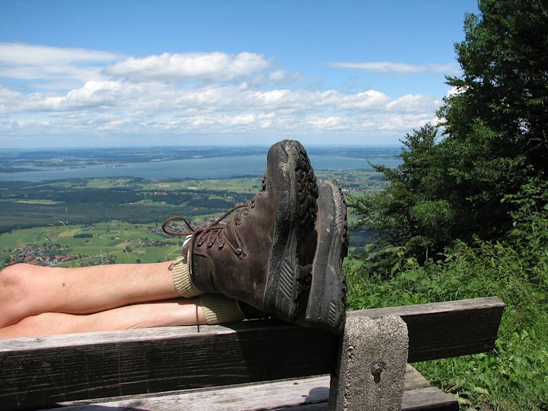 Lower legs in hiking boots resting on the back of a bench in the countryside